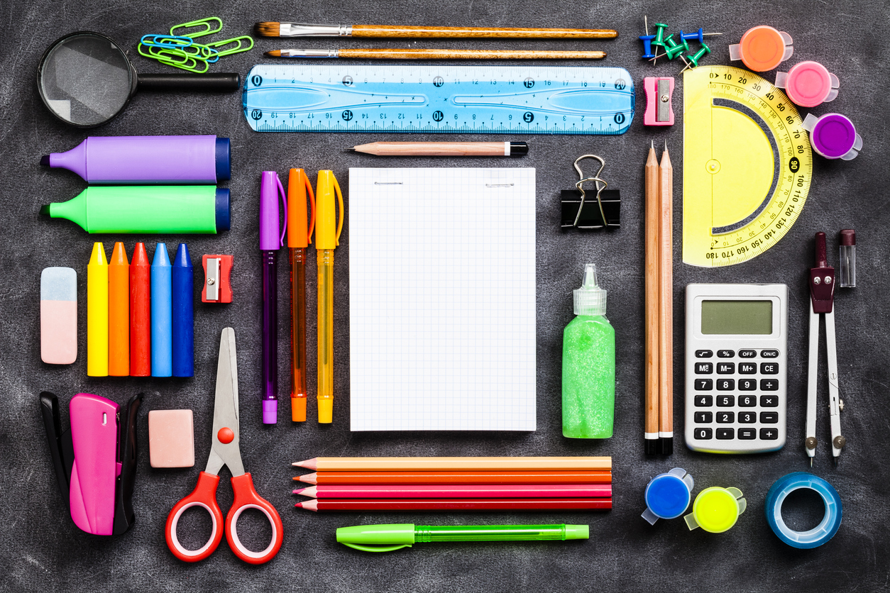 Top view of a large group of multi colored school or office supplies shot on rustic black background. A blank note pad is at the center of the composition with a useful copy space ready for text and/or logo. DSRL studio photo taken with Canon EOS 5D Mk II and Canon EF 100mm f/2.8L Macro IS USM